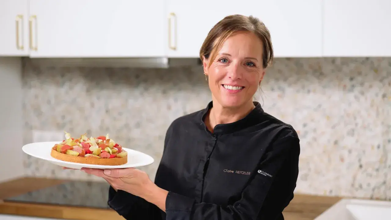 Pâtissière souriante tenant une tartelette aux fruits, peut-être préparée avec de la pectine ou de la gélatine pour une texture parfaite.