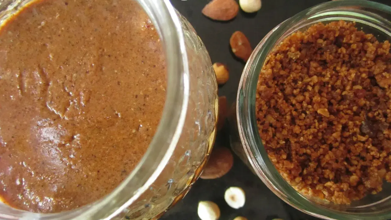 Deux pots de praliné maison, l'un crémeux, l'autre concassé, entourés d'amandes et de noisettes. La conservation est assurée !