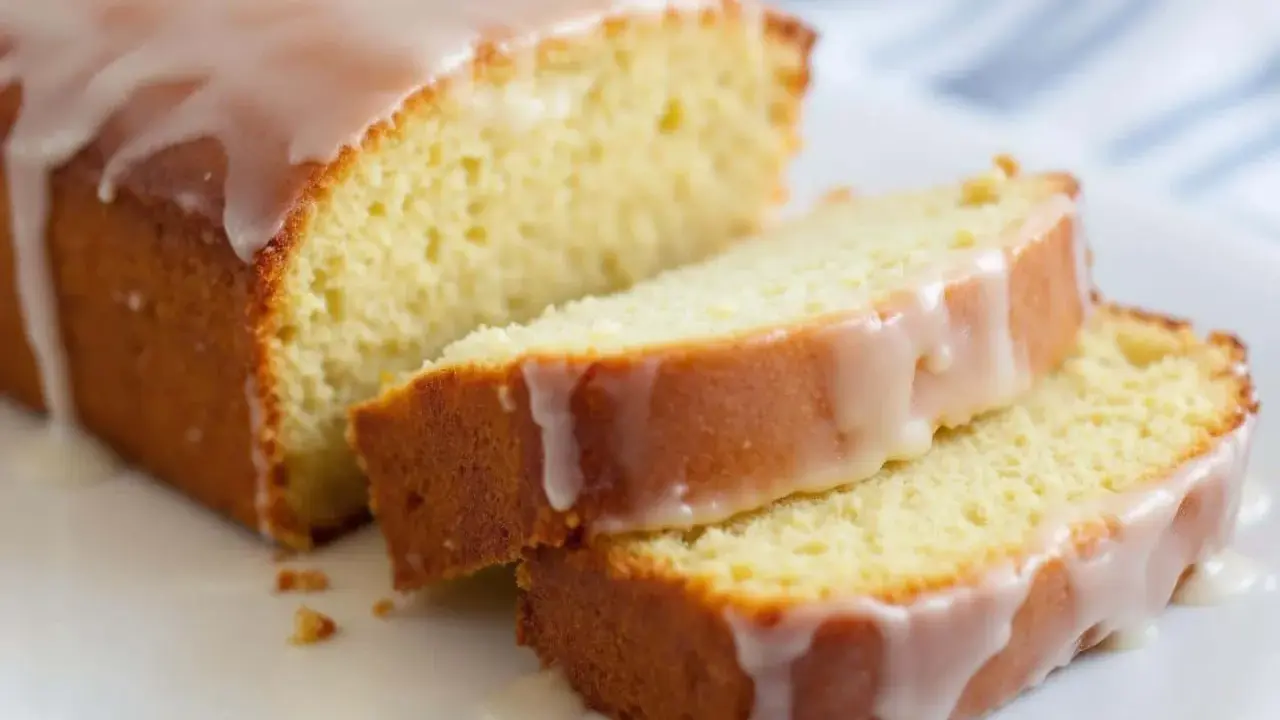 Un délicieux gâteau courgette citron, nappé d'un glaçage blanc, est coupé en tranches sur une assiette blanche.