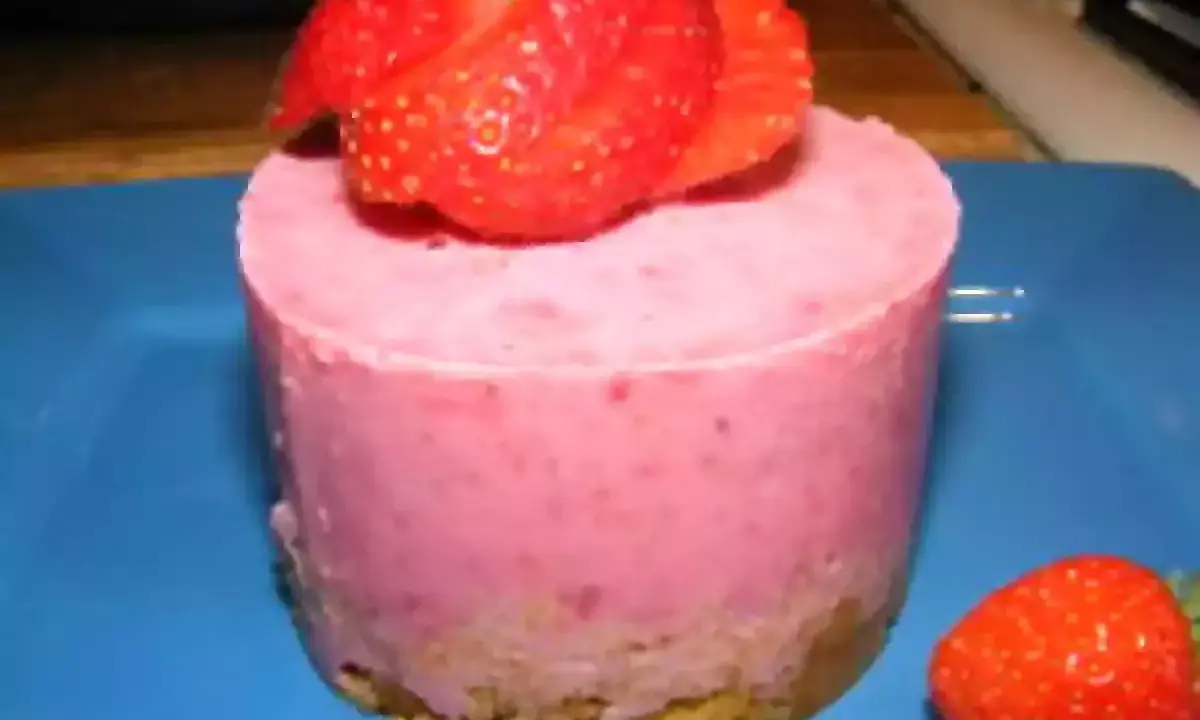 Gâteau individuel rose vif, garni de fraises fraîches. Un délice au glacage fraise sur fond bleu.
