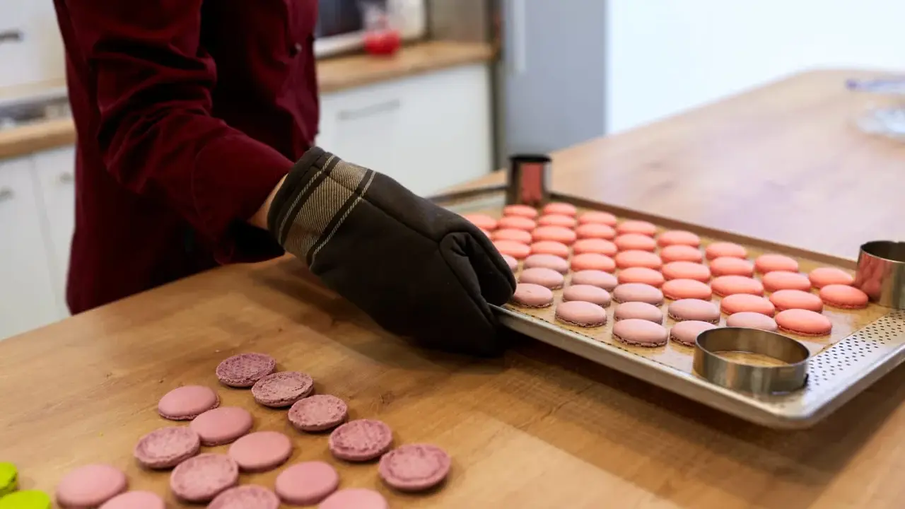 Préparation pour la cuisson macaron four traditionnel : une plaque de macarons roses et roses est prête, des cercles à pâtisserie sont à proximité.