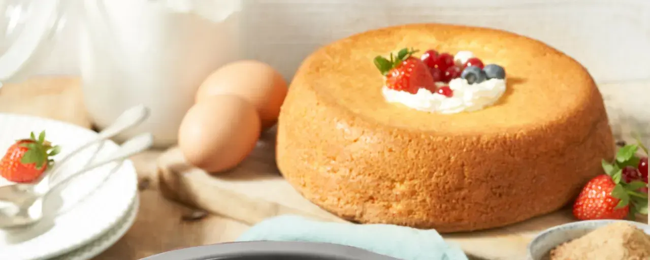 Un savarin traditionnel, doré et moelleux, garni de crème fouettée et de fruits rouges. Des œufs et de la farine sont prêts pour la préparation.