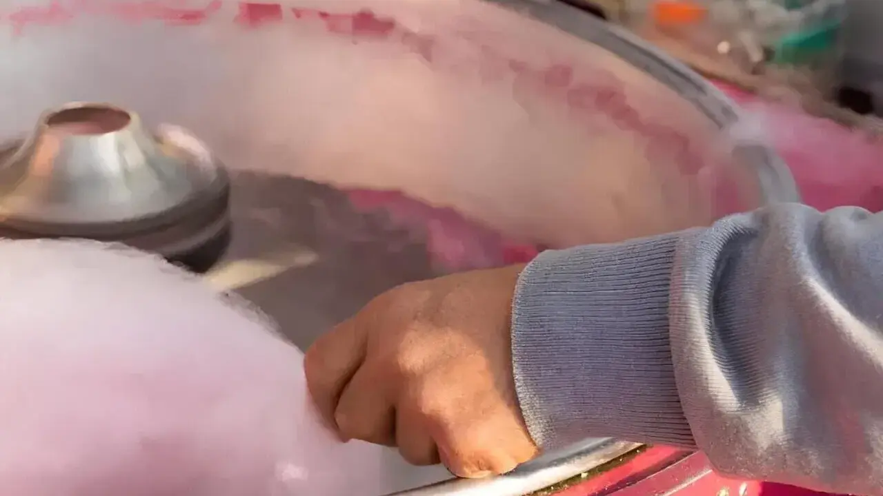Main d'une personne récoltant du sucre filé rose, étape clé pour savoir comment faire du sucre à barbe à papa.