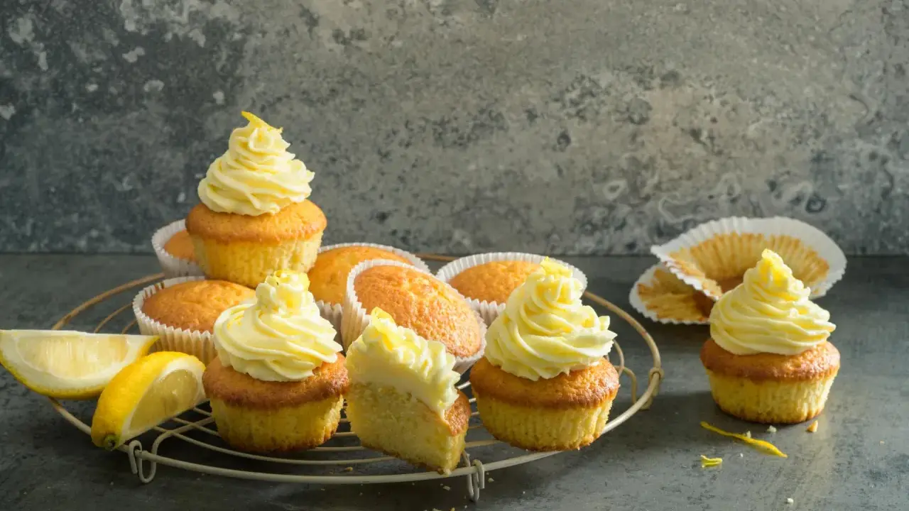 Plusieurs cupcakes citron avec un glaçage jaune vif, certains décorés de zestes. Des quartiers de citron frais sont posés à côté.