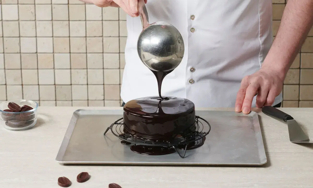 Un chef verse un glaçage au chocolat brillant sur un gâteau rond. Le glaçage sur gâteau froid ou chaud coule parfaitement, créant une finition miroir.