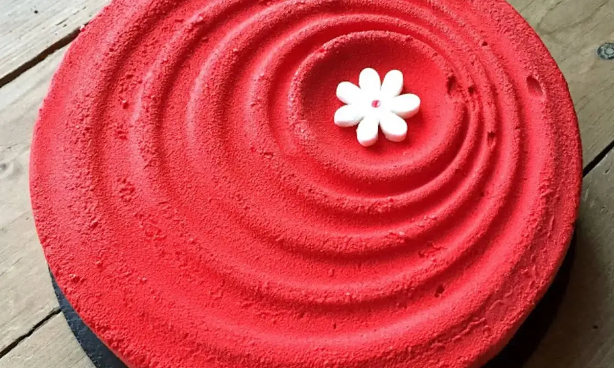 Un tiramisu fraise rhubarbe d'un rouge éclatant, décoré d'une petite fleur blanche en son centre, sur un fond de bois.