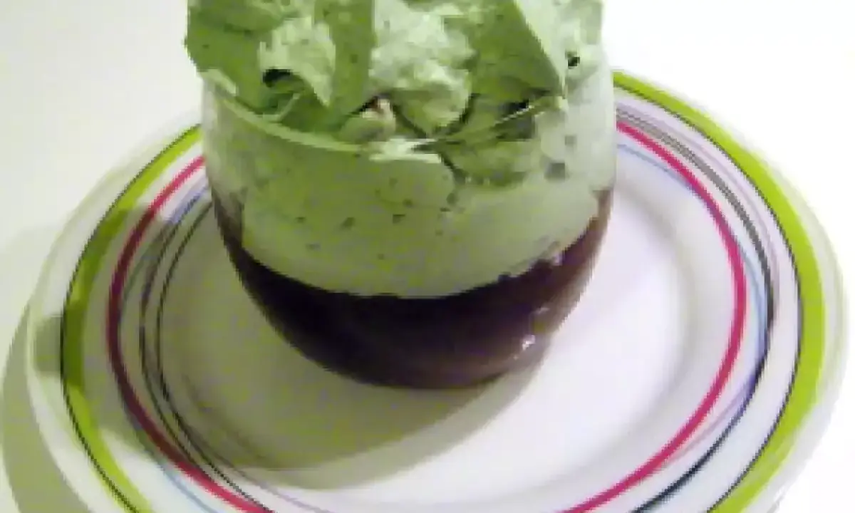 Un verre de dessert avec une couche de chocolat au fond et une généreuse chantilly pistache aérienne sur le dessus, posé sur une assiette colorée.