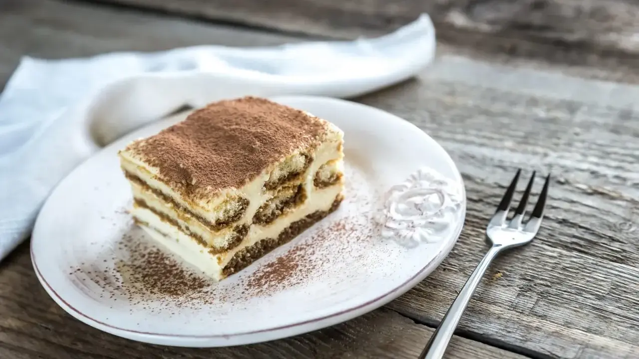 Une part de tiramisu sur une assiette blanche, saupoudrée de cacao. Combien de temps au frigo pour ce délice ?