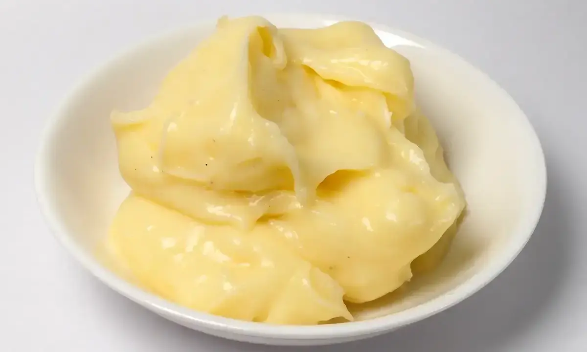 Crème pâtissière onctueuse, légèrement granuleuse, dans un bol blanc. Des points noirs de vanille parsèment la texture crémeuse.