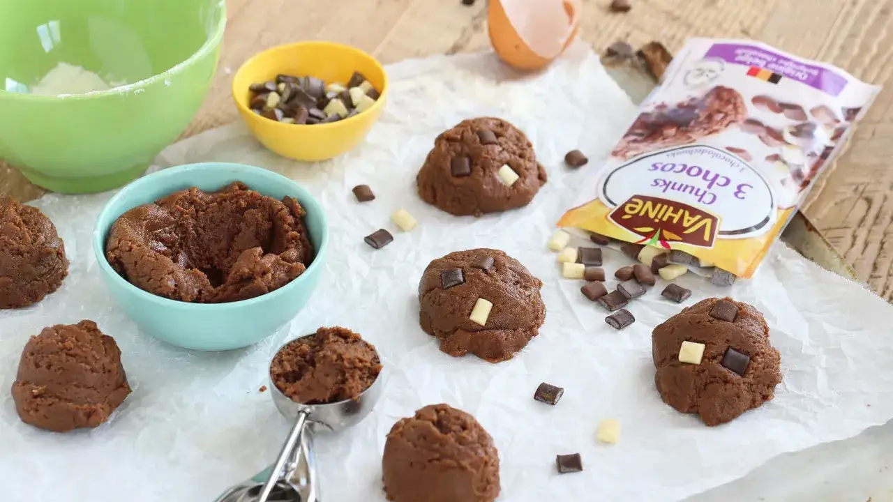 Pâte à cookies au chocolat prête à être façonnée. Des pépites de chocolat et un sachet "comment faire des pépites de chocolat" sont à proximité.