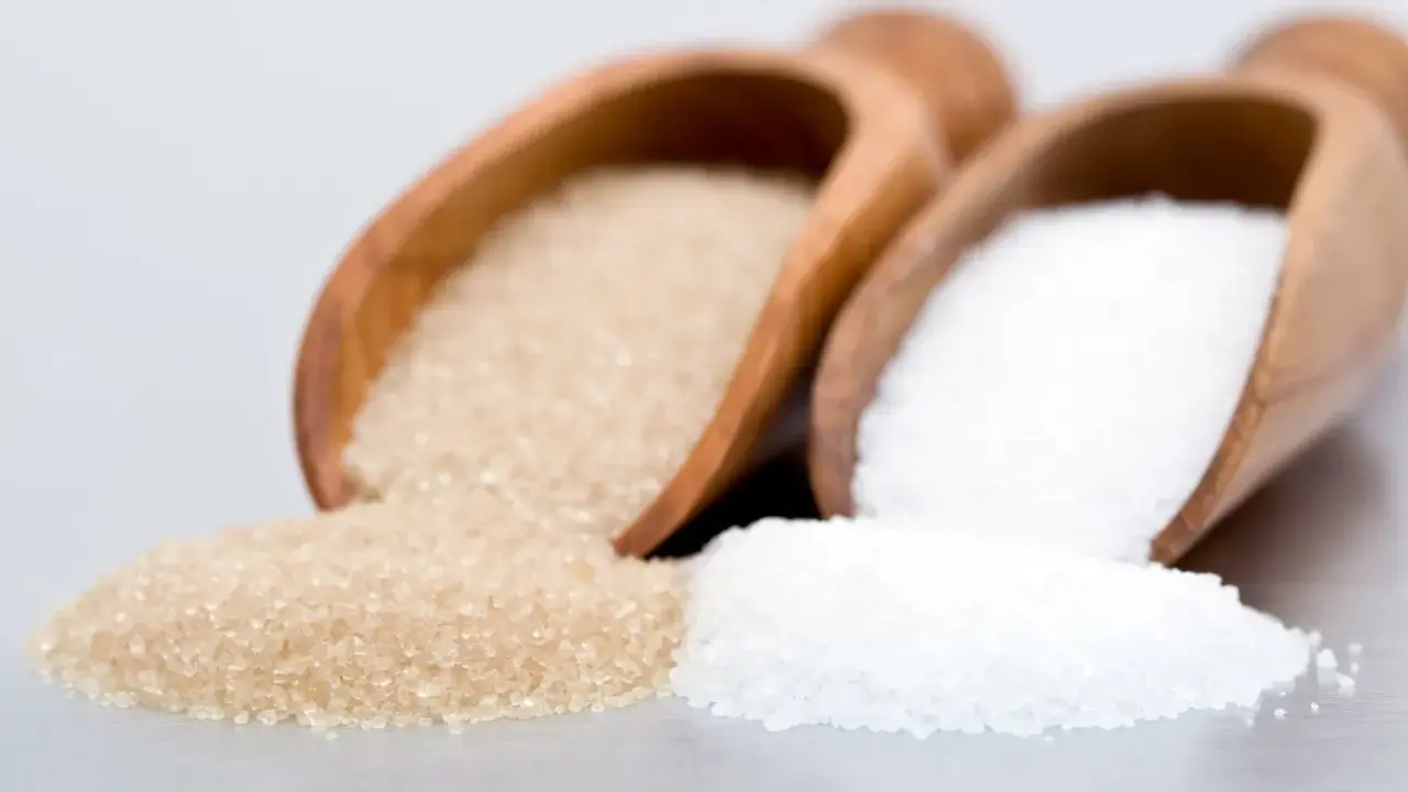 Deux cuillères en bois contiennent différents types de sucre en pâtisserie : du sucre blanc et du sucre roux.