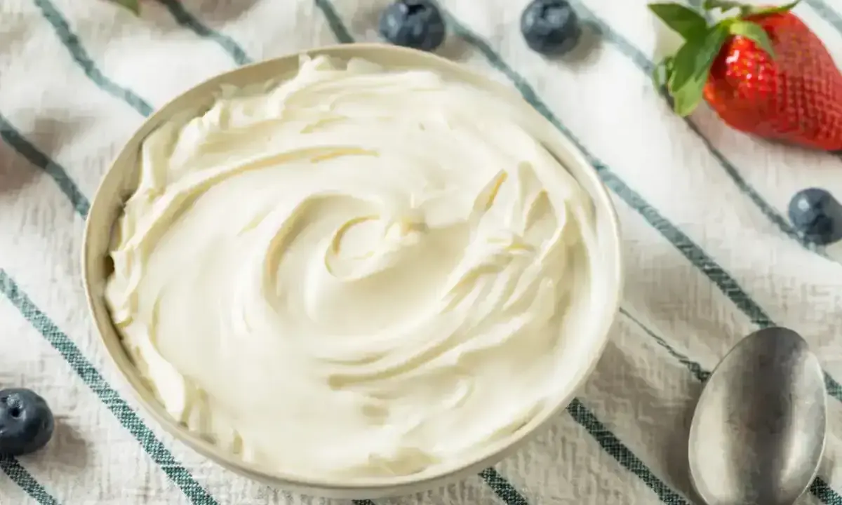 Un bol de crème mascarpone onctueuse, garni de fraises et de myrtilles, prêt à être dégusté.