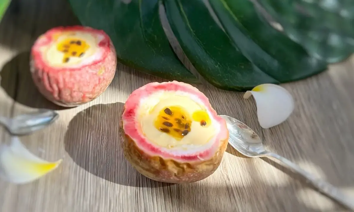 Deux moitiés de fruit de la passion garnies d'une crème jaune et de graines noires, sur une table en bois, avec une feuille tropicale et des pétales de fleurs.