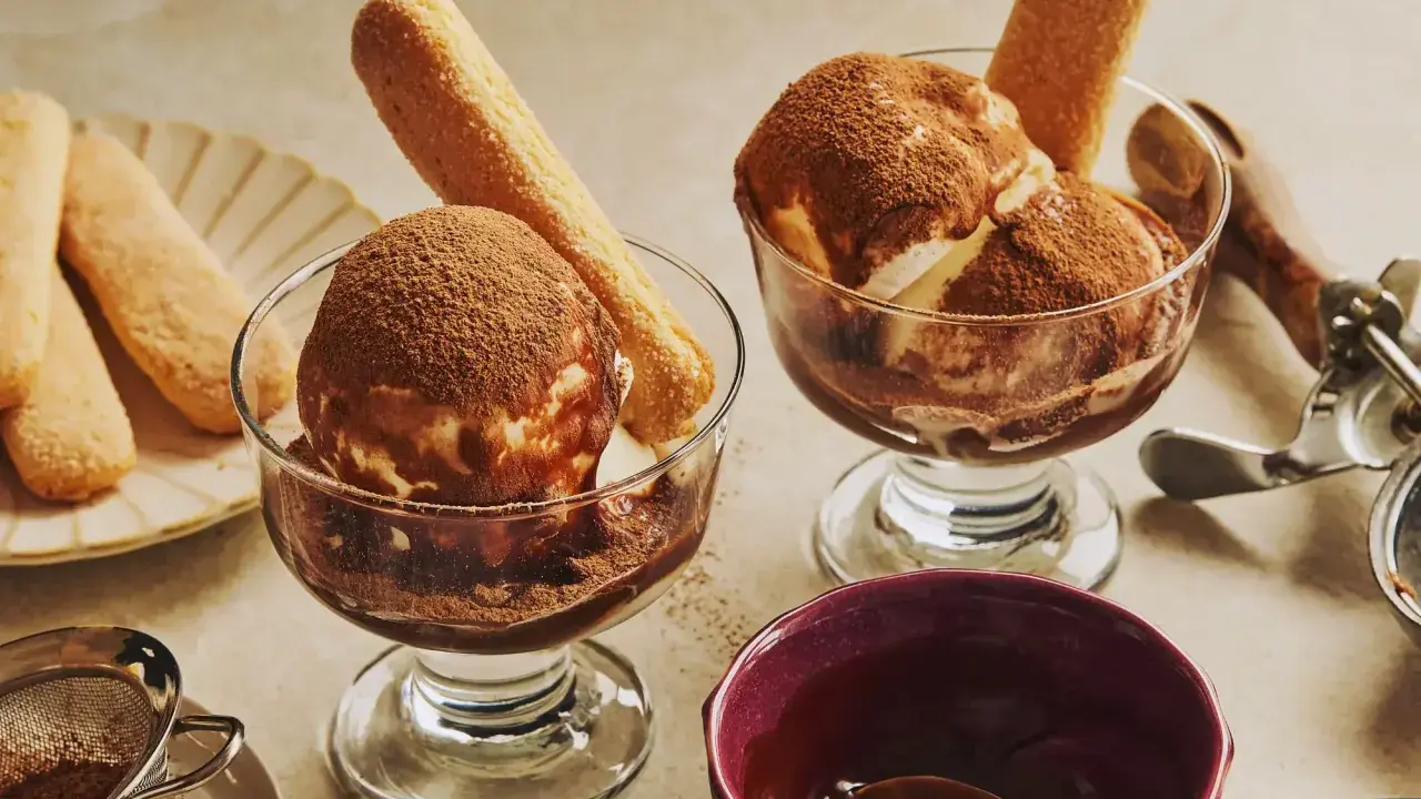 Deux coupes de glace tiramisu, saupoudrées de cacao, avec des biscuits à la cuillère. Un délice glacé à savourer.