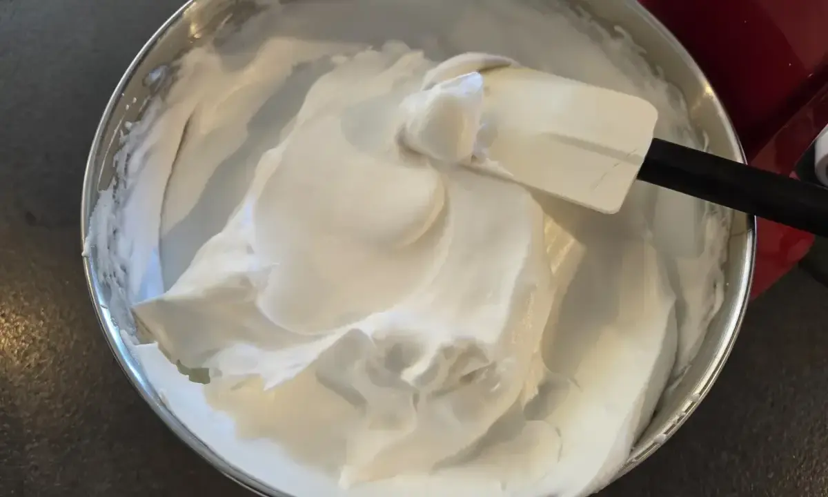 Une spatule mélange une épaisse crème chantilly dans un bol en acier inoxydable.