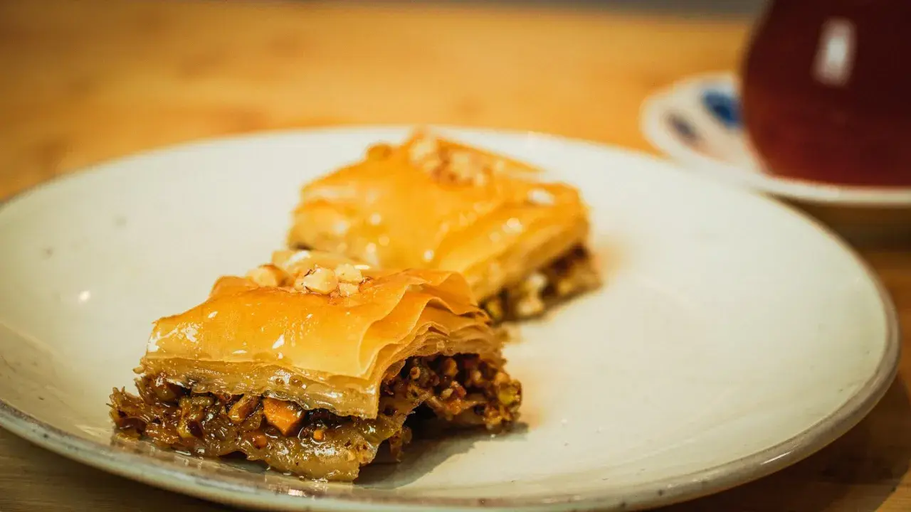 Deux parts de baklava, garnies de noix, sur une assiette. Une recette de baklava qui fait saliver.