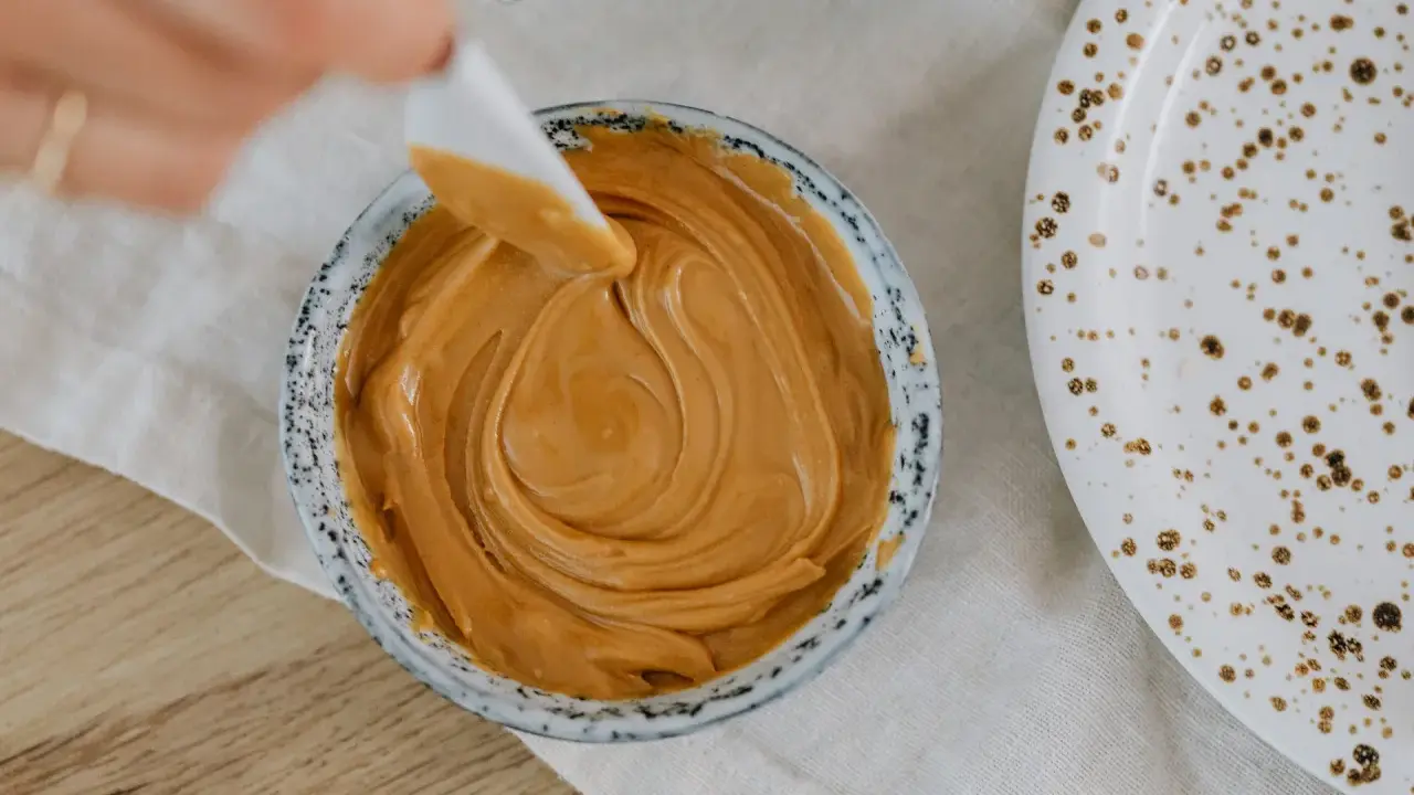 Une spatule prélève une portion de crème d'amandes légère dans un bol. Une assiette tachetée est à côté.