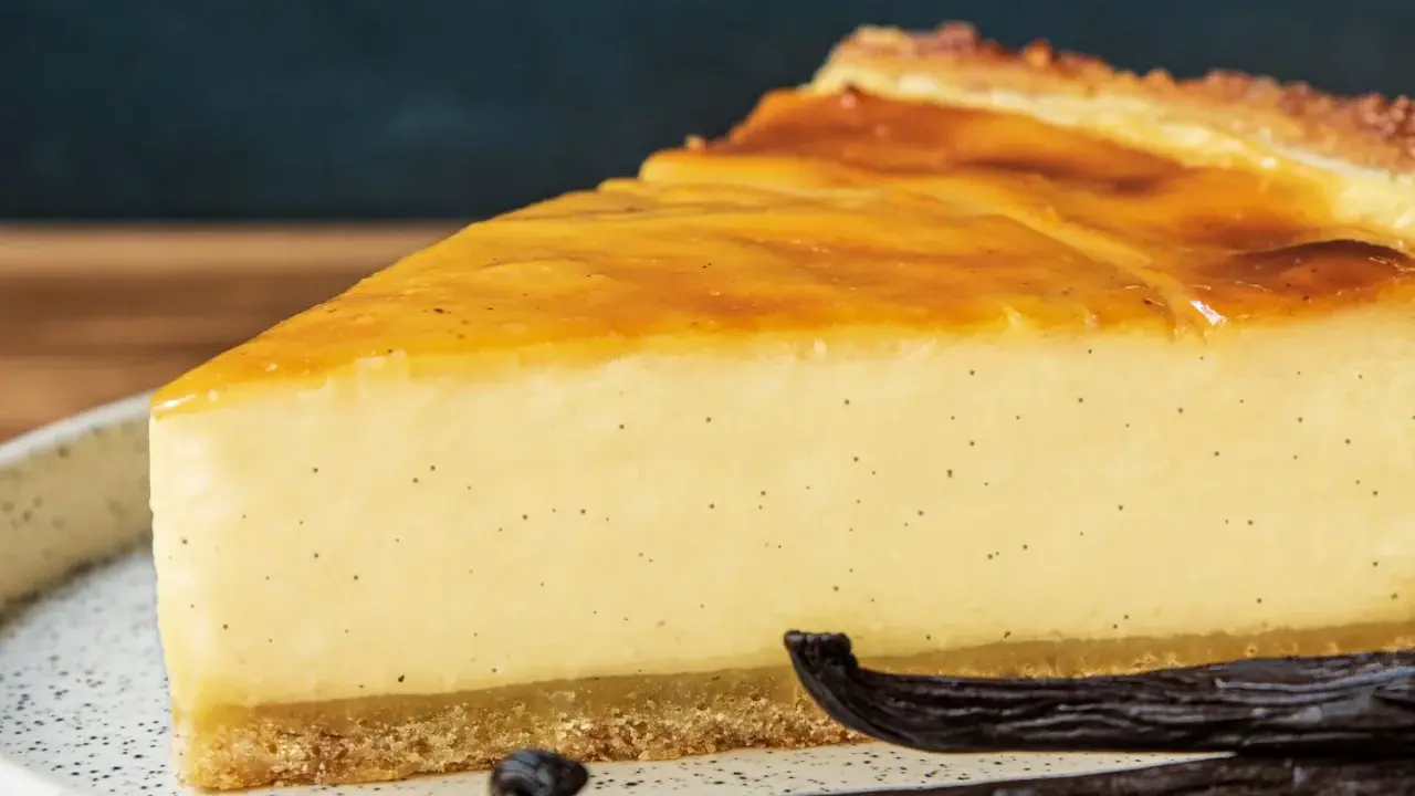 Tranche de flan pâtissier onctueux, parsemé de points de vanille, avec une croûte dorée et des gousses de vanille en premier plan.