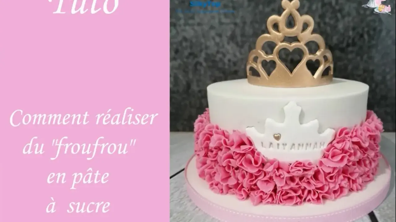 Gâteau d'anniversaire en pâte à sucre blanc orné d'une couronne dorée et d'un "froufrou" rose.
