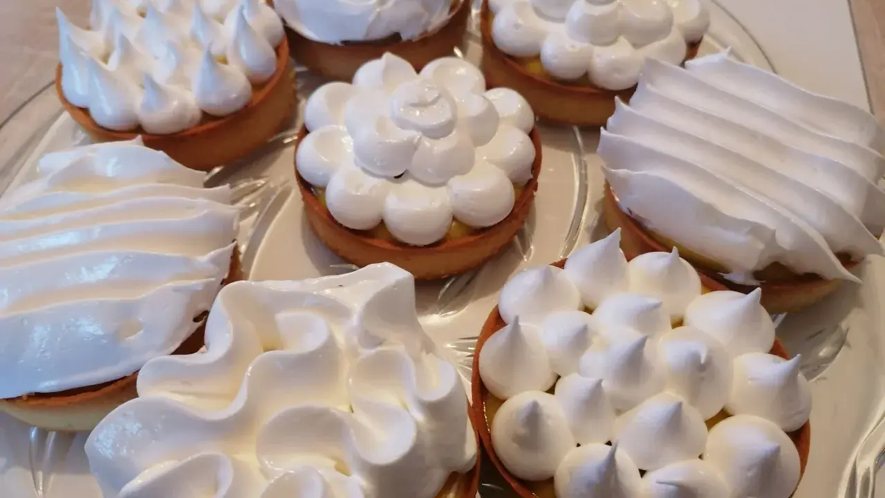 Plusieurs tartelettes garnies de crème citronnée et couronnées de meringue italienne aux formes variées.