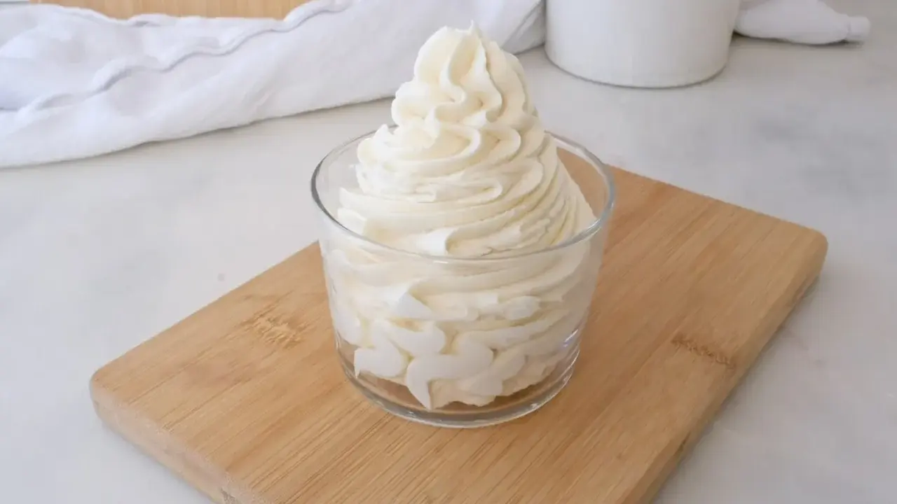 Crème au beurre sucre glace, onctueuse et aérienne, dressée dans un verre sur une planche en bois.