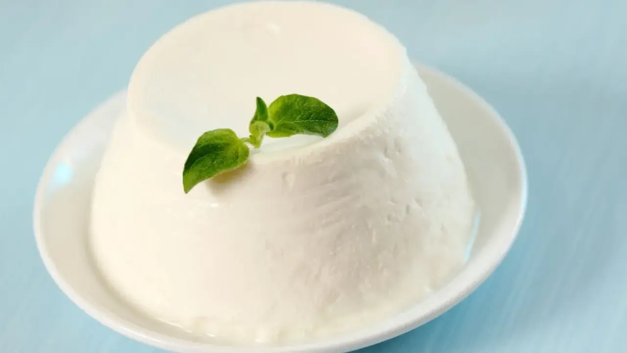 Un dôme de ricotta crémeuse, garni d'une feuille verte, sur une assiette blanche. Découvrez les ricotta bienfaits pour une alimentation saine.