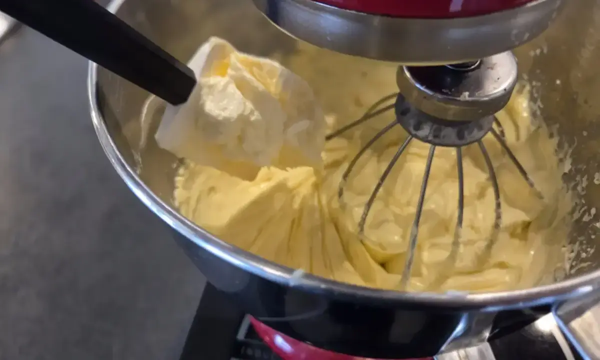 Une spatule ajoute une touche finale à une crème mousseline légère dans un robot pâtissier.