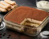Un délicieux tiramisu caramel, généreusement saupoudré de cacao, prêt à être dégusté. Des biscuits à la cuillère et une tasse d'espresso complètent cette gourmandise.