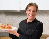 Pâtissière souriante tenant une tartelette aux fruits, peut-être préparée avec de la pectine ou de la gélatine pour une texture parfaite.