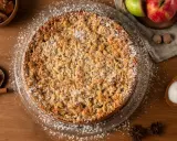 Un délicieux crumble pomme, saupoudré de sucre glace, entouré de pommes fraîches, de noix de muscade et de bâtons de cannelle.