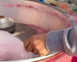 Main d'une personne récoltant du sucre filé rose, étape clé pour savoir comment faire du sucre à barbe à papa.