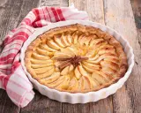 Tarte aux pommes dorée, décorée de bâtons de cannelle et d'anis étoilé. Une serviette à carreaux rouges et blancs est posée à côté. Idéale pour la conservation.