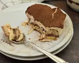 Une part de tiramisu nutella, saupoudrée de cacao, sur une assiette. Une cuillère en argent a prélevé un morceau crémeux.