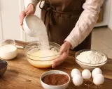 Préparation d'un gâteau : on verse du sucre dans un bol, une alternative pour remplacer le sucre blanc. Ingrédients : œufs, lait, farine, cacao, chocolat.
