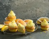 Plusieurs cupcakes citron avec un glaçage jaune vif, certains décorés de zestes. Des quartiers de citron frais sont posés à côté.