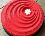 Un tiramisu fraise rhubarbe d'un rouge éclatant, décoré d'une petite fleur blanche en son centre, sur un fond de bois.