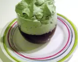 Un verre de dessert avec une couche de chocolat au fond et une généreuse chantilly pistache aérienne sur le dessus, posé sur une assiette colorée.