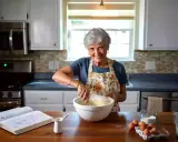 Une grand-mère souriante prépare une pâte. Elle sait à quoi sert la levure chimique : à rendre ses gâteaux légers et aériens !