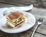 Une part de tiramisu sur une assiette blanche, saupoudrée de cacao. Combien de temps au frigo pour ce délice ?
