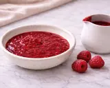 Un bol et un pichet remplis de nappage framboise facile, avec des framboises fraîches à côté.