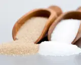 Deux cuillères en bois contiennent différents types de sucre en pâtisserie : du sucre blanc et du sucre roux.