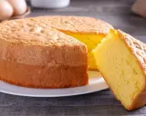 Un moelleux gâteau de Savoie, parfait pour la conservation, avec une part coupée. Des œufs et un fouet en arrière-plan suggèrent sa préparation.