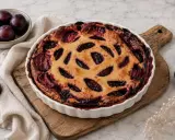 Un délicieux clafoutis aux prunes, doré et garni de fruits juteux, est prêt à être dégusté. Quelques prunes fraîches l'accompagnent.