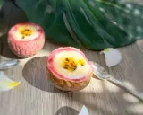 Deux moitiés de fruit de la passion garnies d'une crème jaune et de graines noires, sur une table en bois, avec une feuille tropicale et des pétales de fleurs.