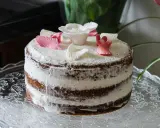 Un délicieux layer cake fleuri, avec des pétales de roses en sucre roses et blancs, posé sur un plat en verre orné.