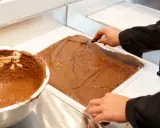 Un chef étale une pâte chocolatée onctueuse dans un moule. C'est la base du praliné, une gourmandise qui fait rêver.