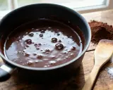 Comment faire fondre du chocolat : une casserole de chocolat fondu, du cacao en poudre, du sucre et une spatule en bois sur une table en bois.