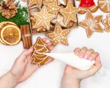 Mains décorant un biscuit sapin avec du glaçage royal. Autour, des étoiles et des décorations de Noël.