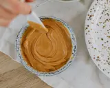 Une spatule prélève une portion de crème d'amandes légère dans un bol. Une assiette tachetée est à côté.