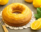Gâteau moelleux au mascarpone et citron, prêt à être dégusté. Des citrons frais et une touche de verdure complètent la scène.